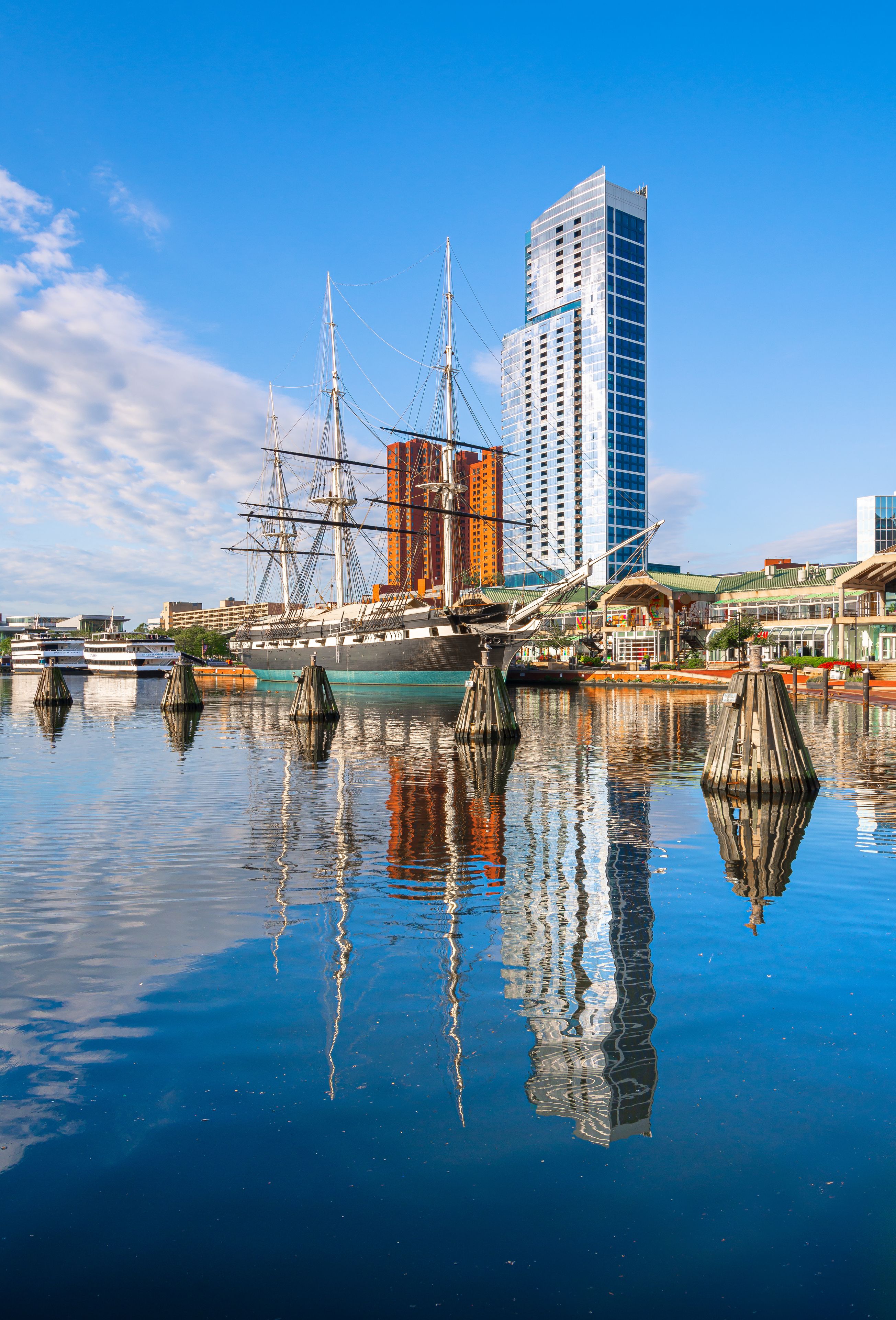 A historic sailing ship docked at a modern waterfront with tall buildings in the background.