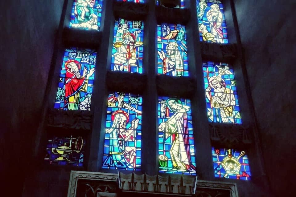 Uma janela de vitrais com figuras religiosas e uma estátua abaixo.