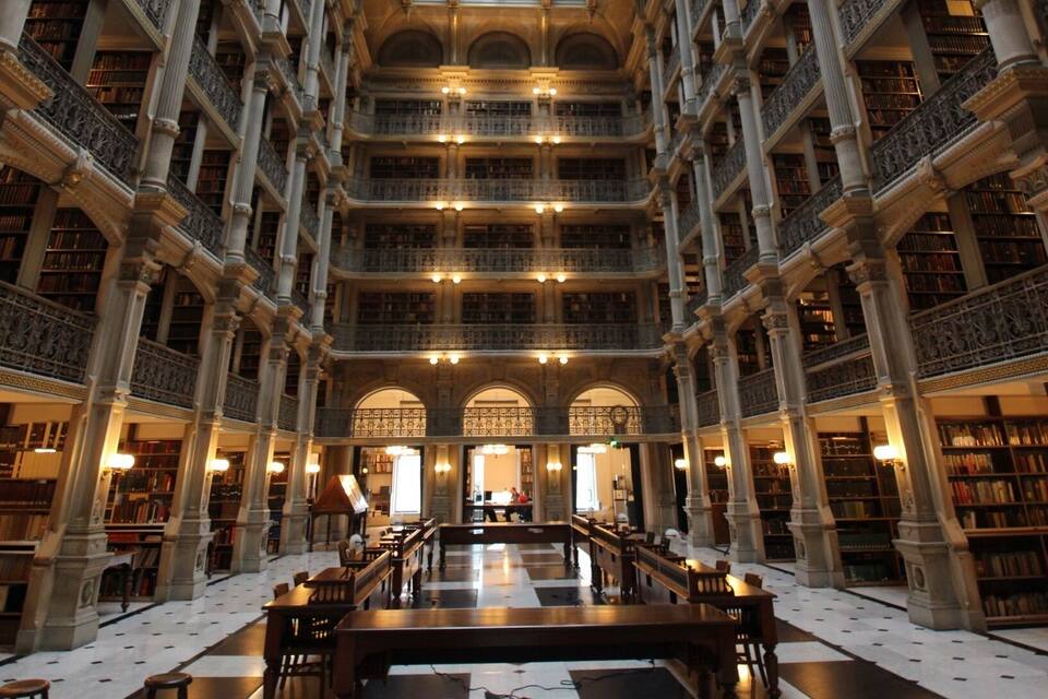 Una biblioteca imponente con techo alto, barandillas ornamentadas y suelo a cuadros.