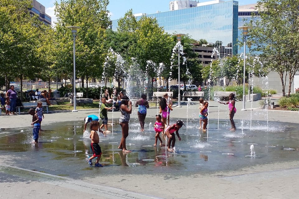 Un parc públic amb una zona de font i persones que hi juguen.