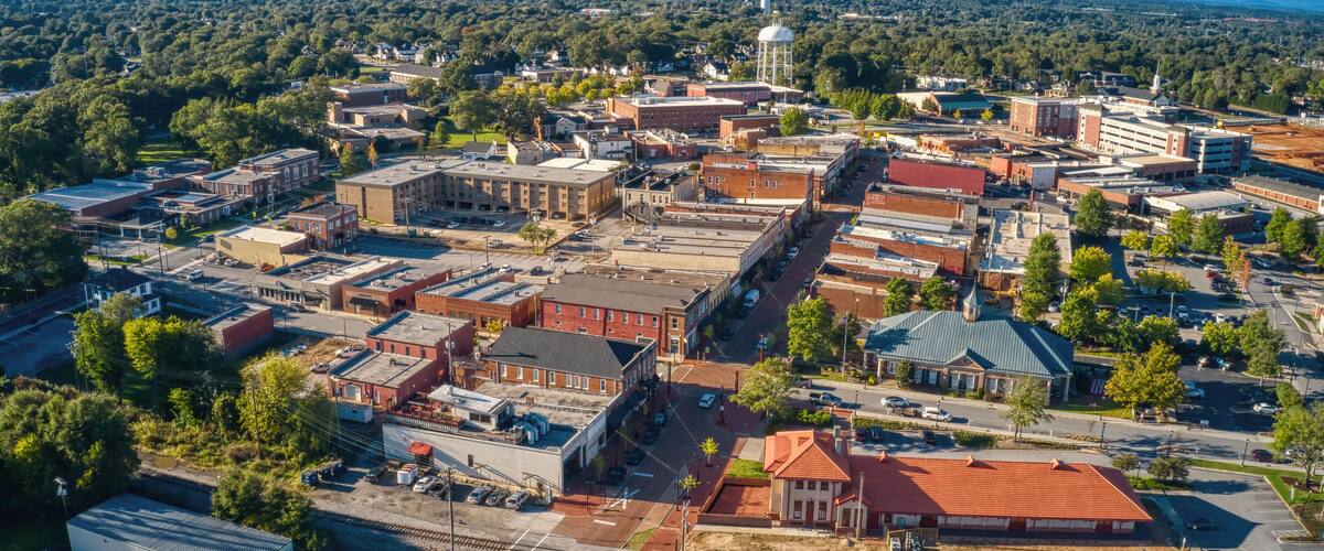 An aerial view of a town with a prominent water tower, a train station, and a mix of commercial and residential buildings.