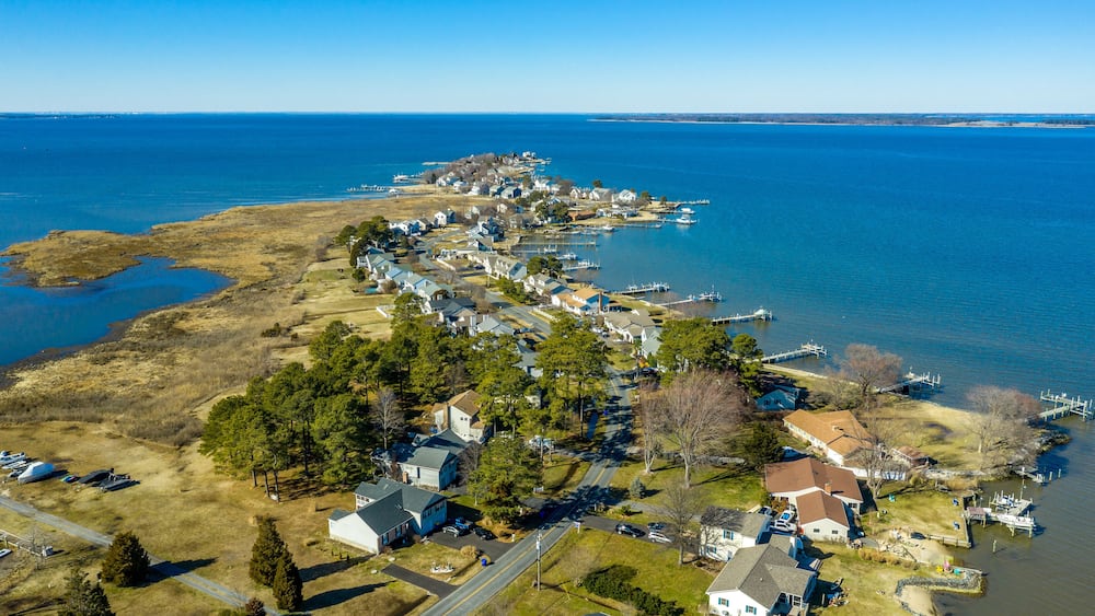 Aerial view of Kent Narrows peninsula inlet on Chesapeake in Grasonville Maryland, beach houses with private long docks for the sailboats line a road curving like an S shape with blue sky and water
