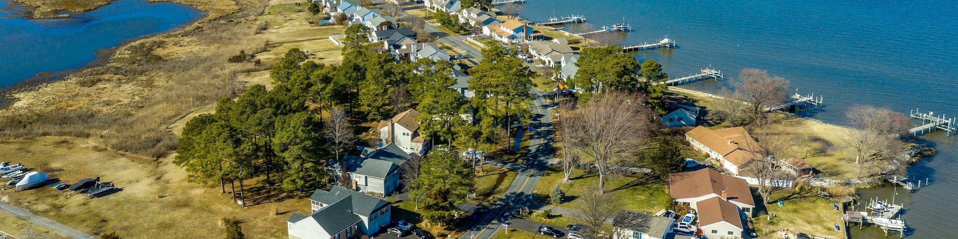 Aerial view of Kent Narrows peninsula inlet on Chesapeake in Grasonville Maryland, beach houses with private long docks for the sailboats line a road curving like an S shape with blue sky and water