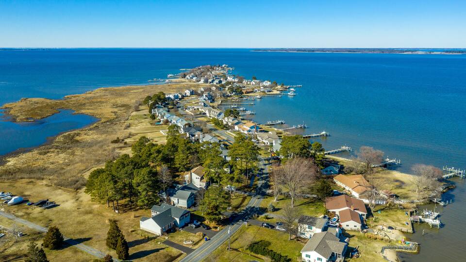 An aerial view of a coastal residential area with houses, docks, and a clear blue sky.