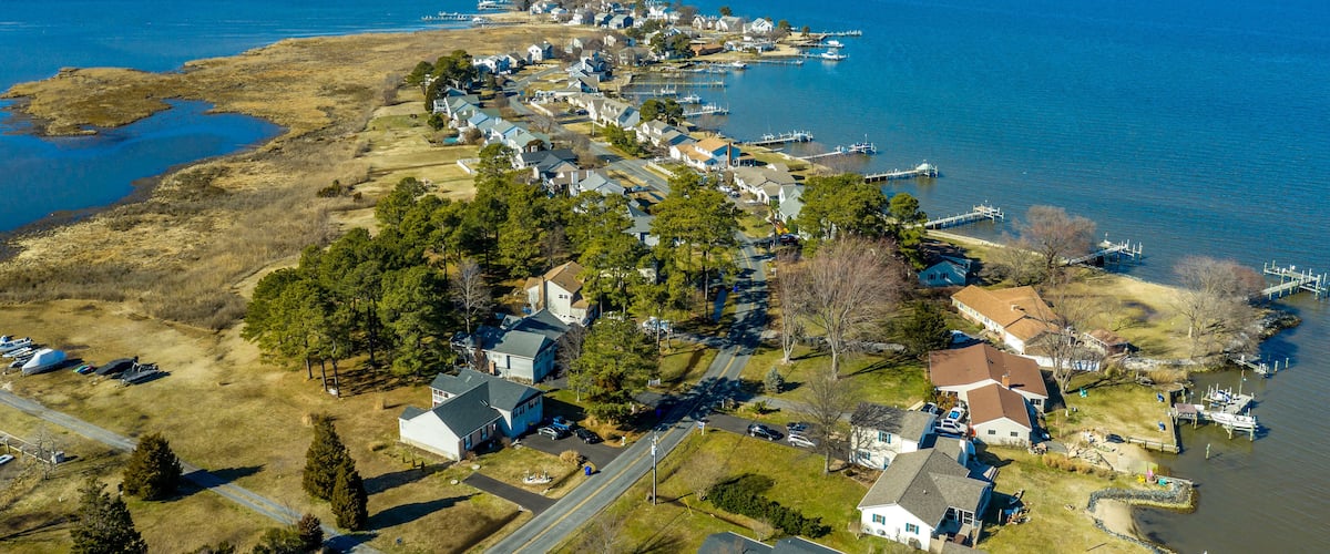 Aerial view of Kent Narrows peninsula inlet on Chesapeake in Grasonville Maryland, beach houses with private long docks for the sailboats line a road curving like an S shape with blue sky and water