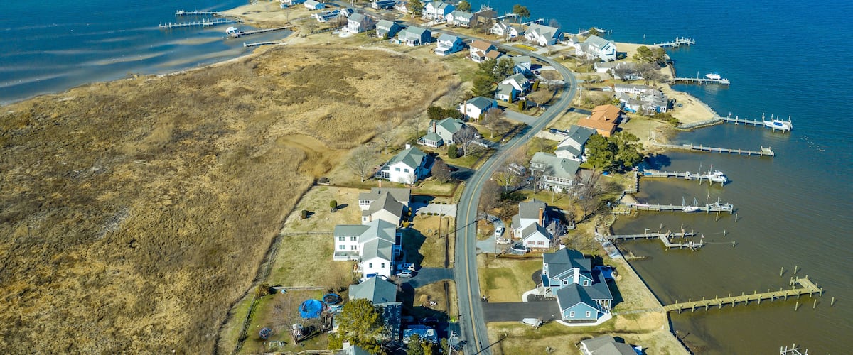 Aerial view of Kent Narrows peninsula inlet on Chesapeake in Grasonville Maryland, beach houses with private long docks for the sailboats line a road curving like an S shape with blue sky and water