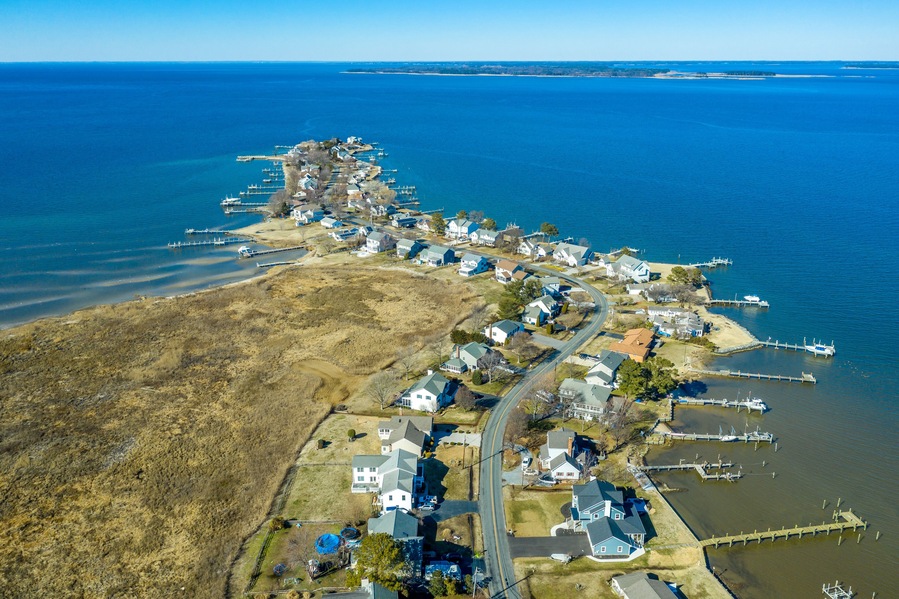 Aerial view of Kent Narrows peninsula inlet on Chesapeake in Grasonville Maryland, beach houses with private long docks for the sailboats line a road curving like an S shape with blue sky and water