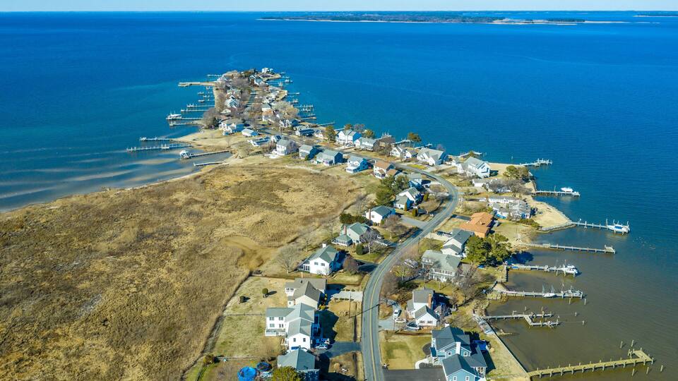 An aerial view of a coastal town with houses, docks, and a road along the shoreline.