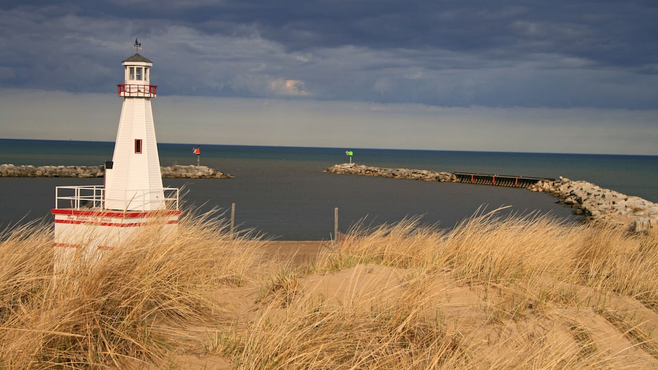A lighthouse on a sandy beach with a rocky breakwater and a cloudy sky.