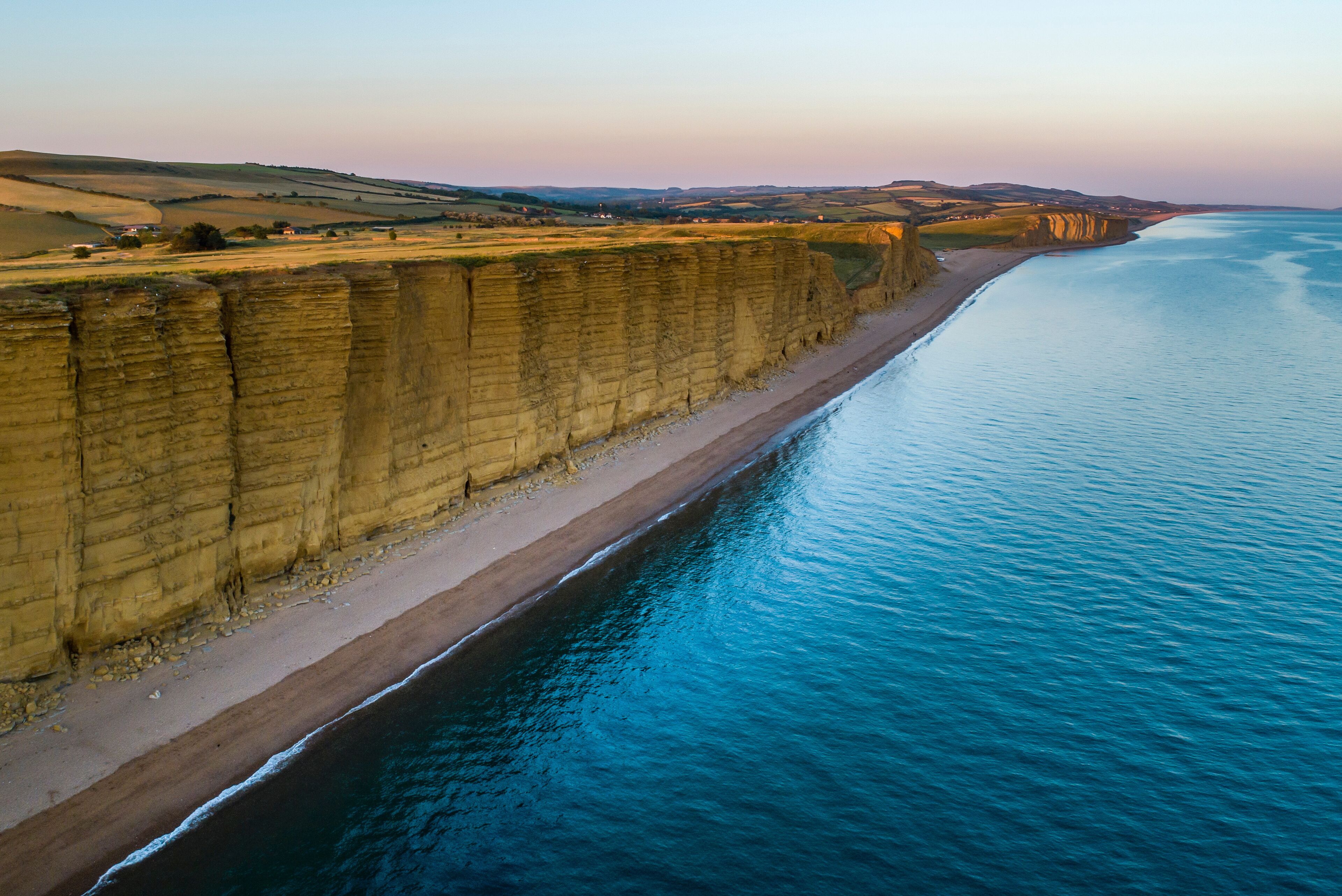 A coastal cliff with a beach and a calm sea.