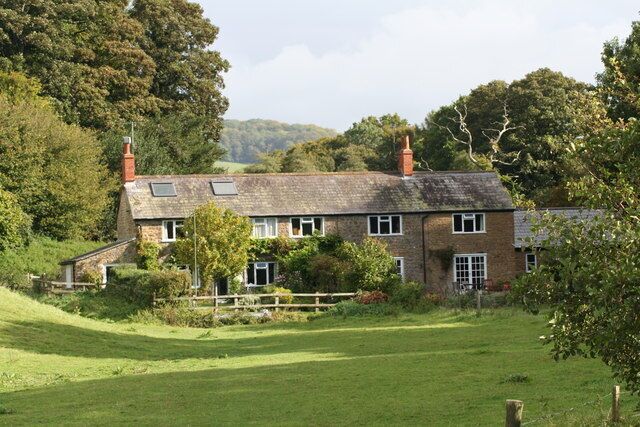 A traditional brick house with a sloped roof, surrounded by a lush green field and trees.