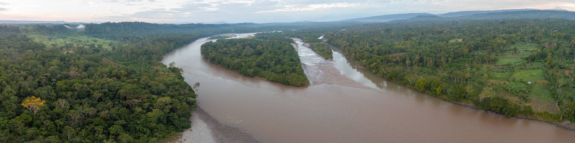 Aerial panorama of the Rio Napo in the Ecuadorian Amazon surrounded by pristine rainforest. A farm cut out of the forest on the right bank.