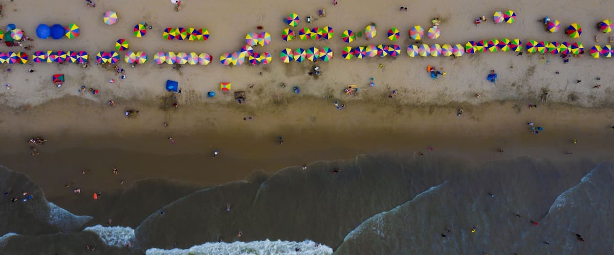 Aerial top view of colorful parasols and many tourist on a beautiful beach: a holiday background of families relaxing in the ocean during vacation