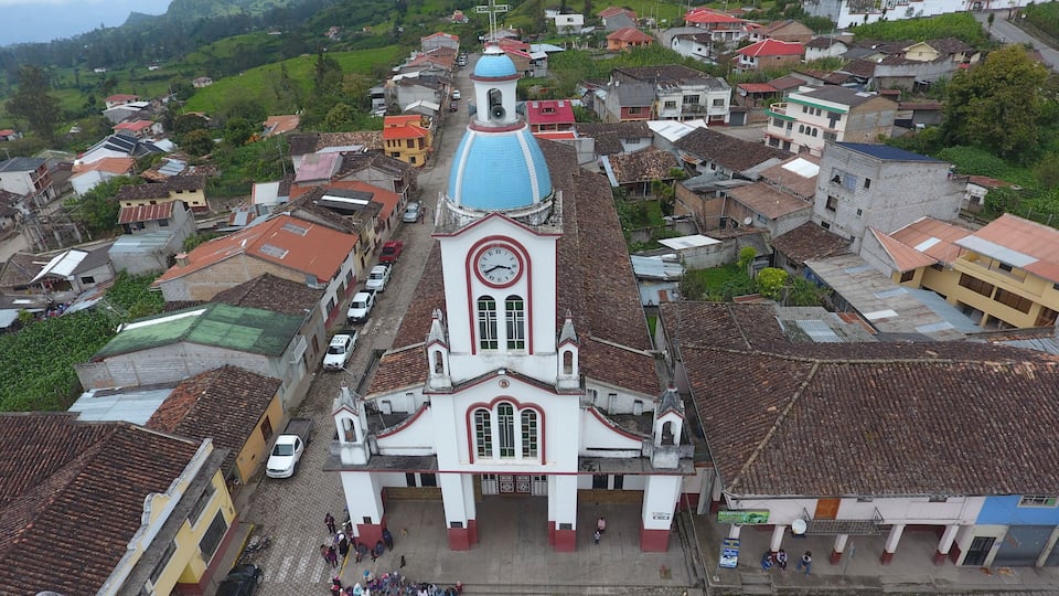 A church with a blue dome and a clock tower in a small town with red-roofed buildings.