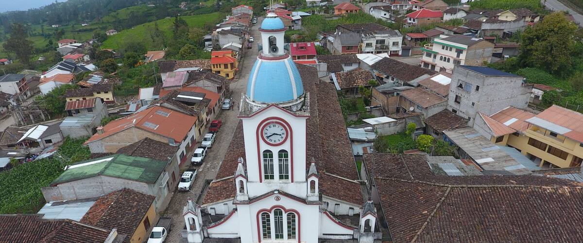 A church with a blue dome and a clock tower in a small town with red-roofed buildings.