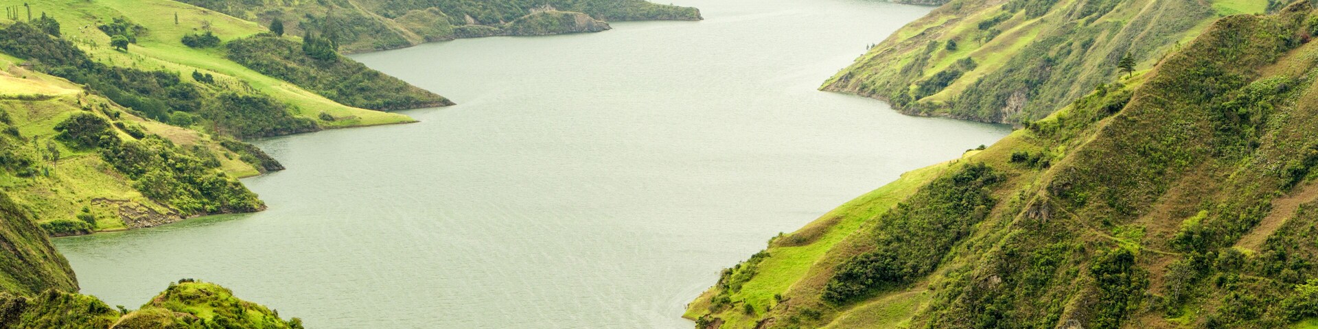 A serene lake in Ecuador's Morona province, surrounded by lush greenery, with the towering Santiago Dam dominating the landscape.