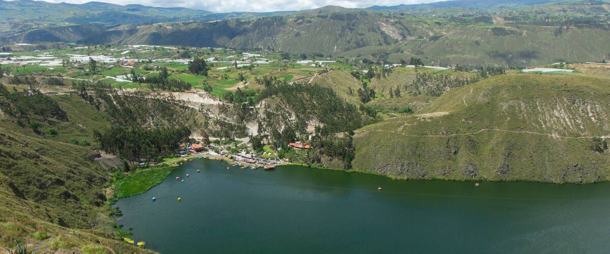 A lake surrounded by hills and a small village with houses and boats.
