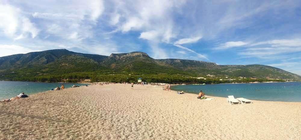 A sandy beach with people and mountains in the background.