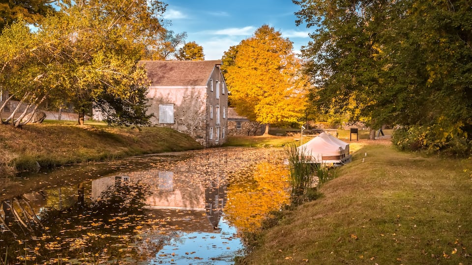 A historic building with a pond reflecting the surrounding trees and a small gazebo.