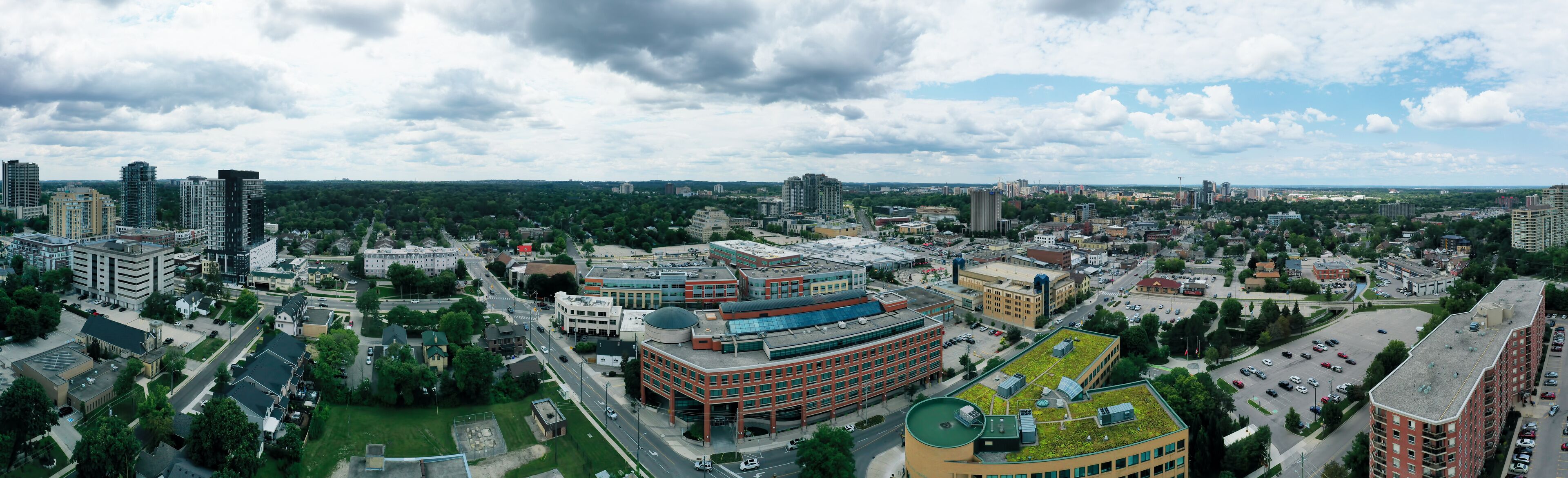 A cityscape with a mix of modern and older buildings, a large green-roofed building, and a cloudy sky.