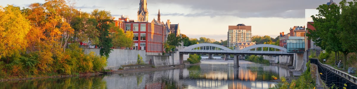 A river with a bridge, a church spire, autumn trees, and urban buildings.