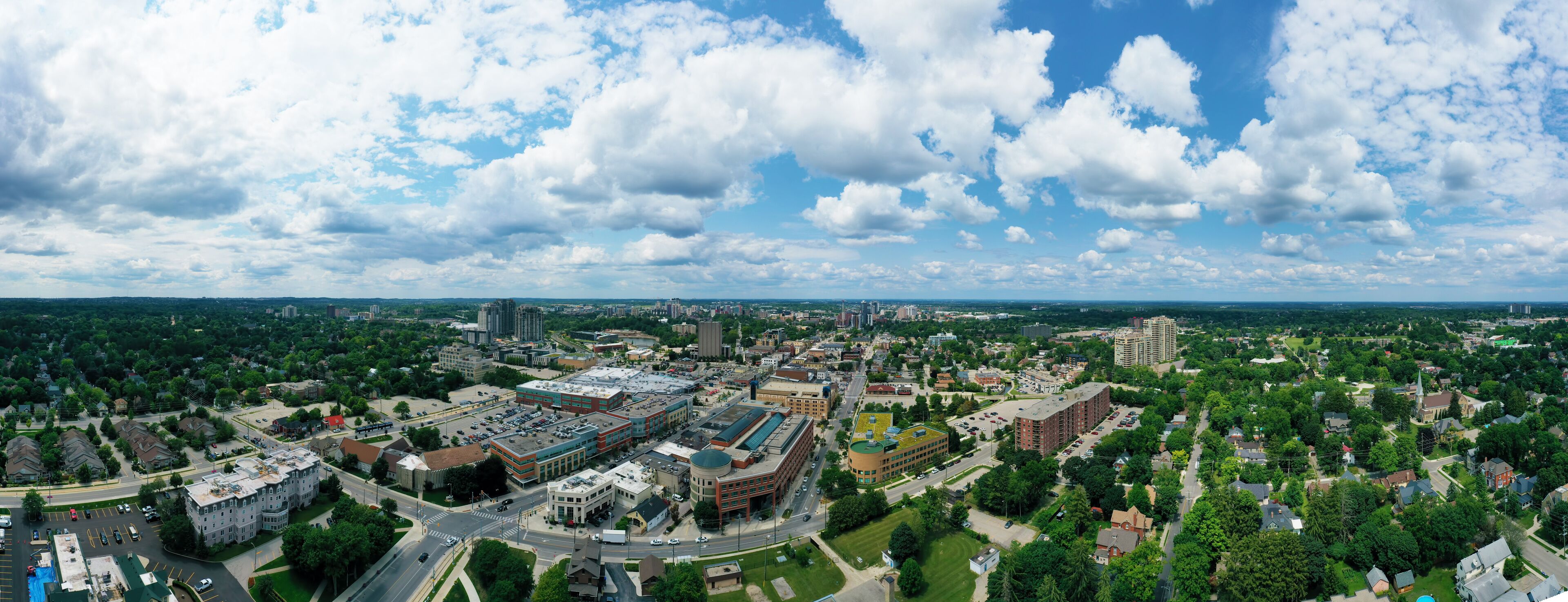 A cityscape with a mix of commercial and residential buildings, surrounded by green areas and a partly cloudy sky.