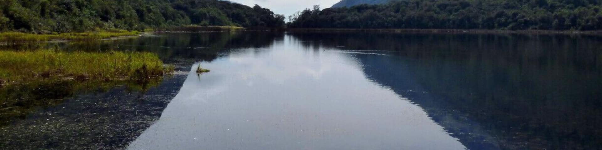 A calm river flanked by lush green mountains under a cloudy sky.