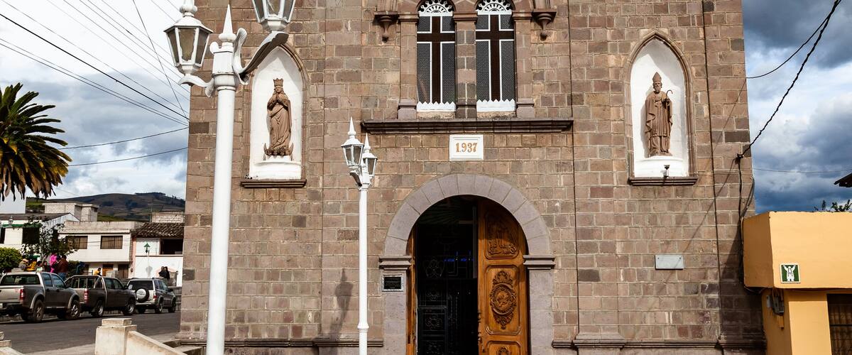 A historic church with a bell tower, a statue, and a tiled entrance.