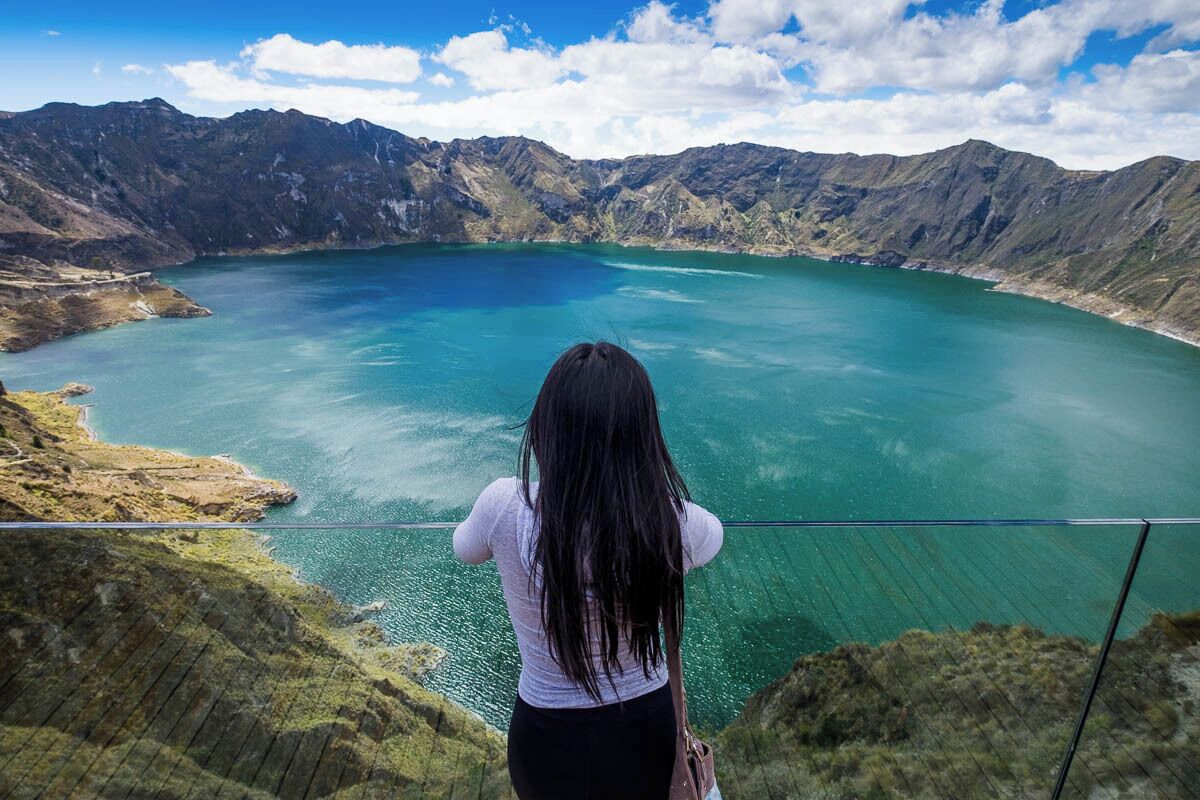 A person overlooking a turquoise lake surrounded by mountains.