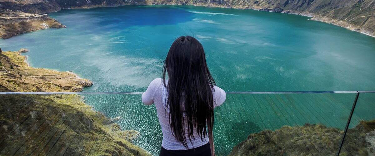 A person overlooking a turquoise lake surrounded by mountains.
