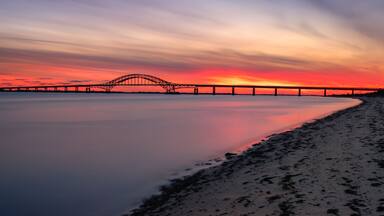 A sunset over a bridge with calm water reflecting the sky.