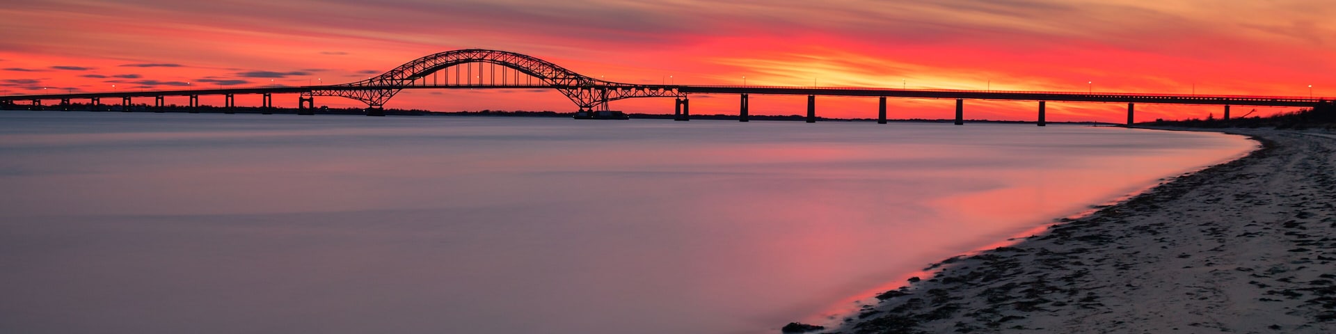 A sunset over a bridge with calm water reflecting the sky.