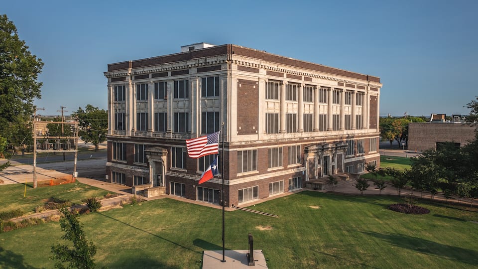 A historic building with a large American flag and a Texas state flag.