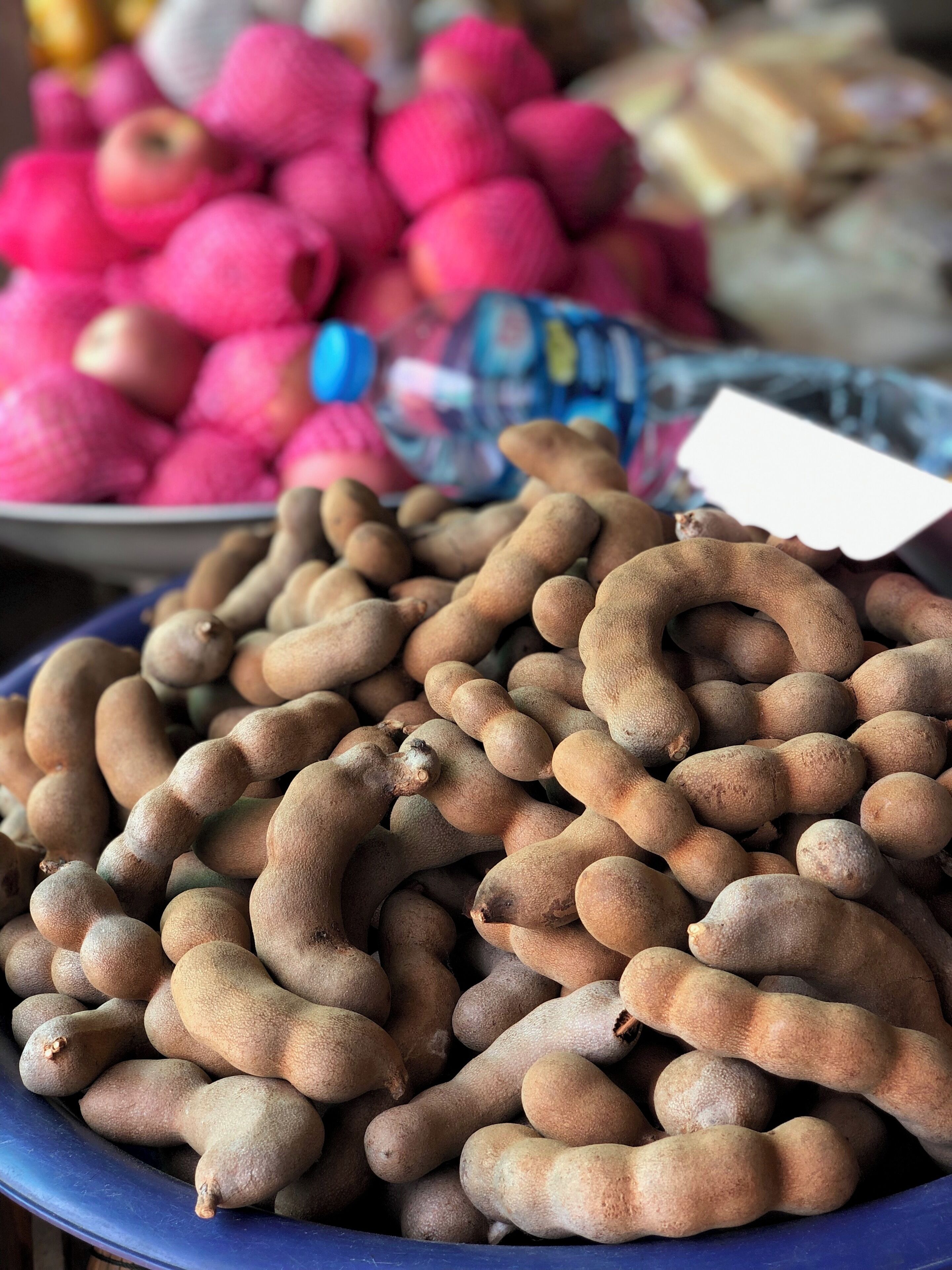A market stall with a blue bowl filled with brown, curved root vegetables.