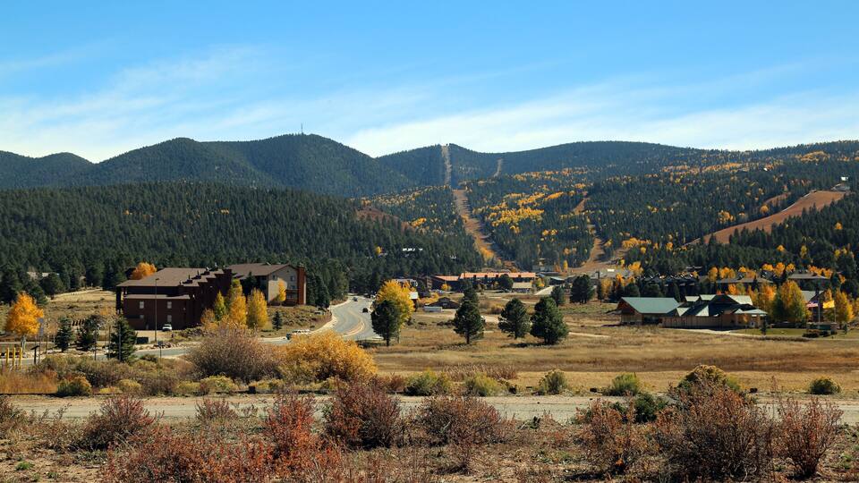 A mountainous landscape with autumn-colored trees, a road, and buildings in the valley.