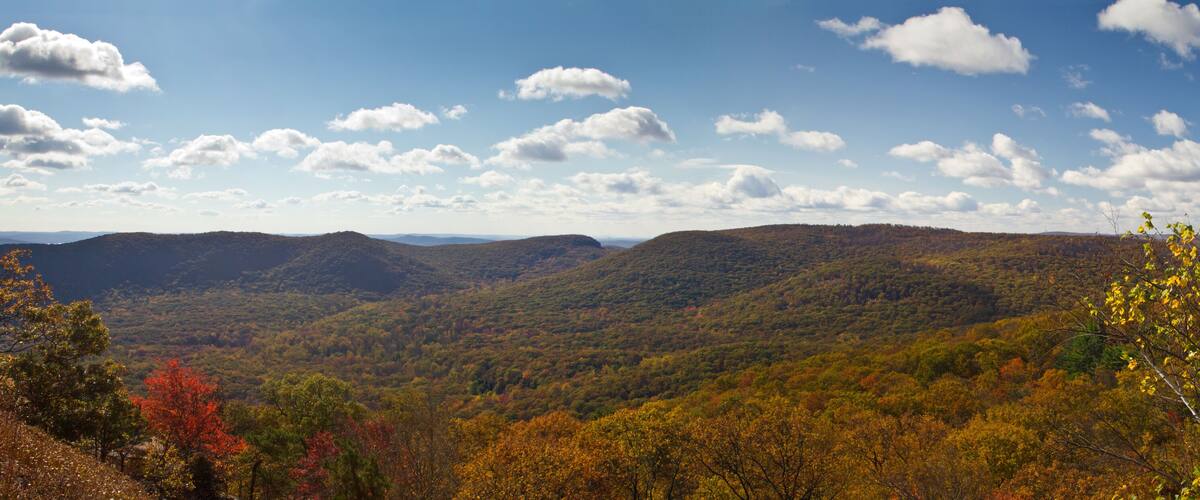 A mountainous landscape with autumn foliage and scattered clouds.