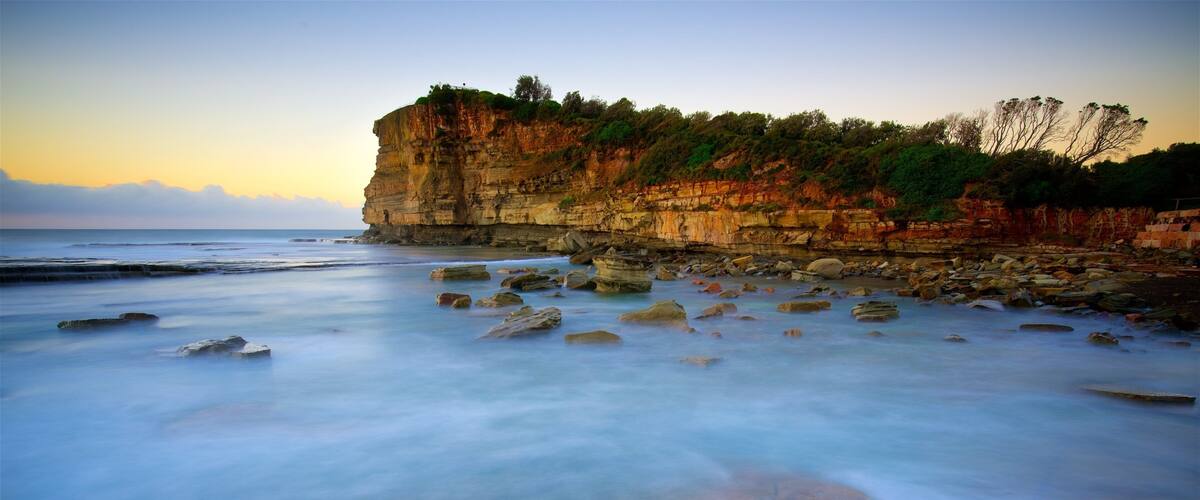 A coastal landscape with a rocky cliff and calm sea.