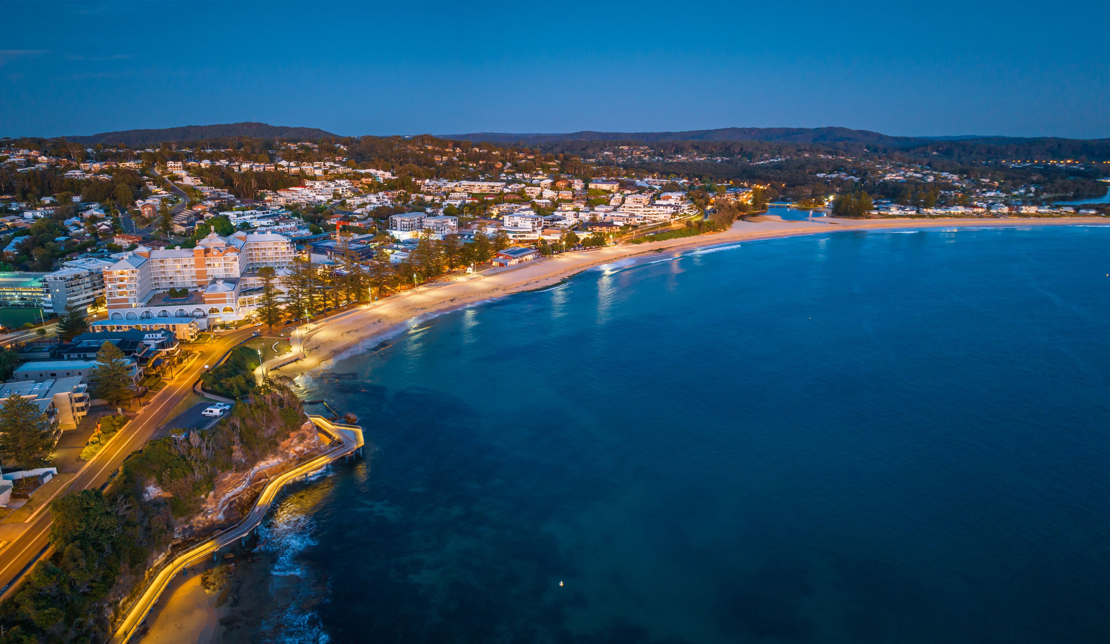 A coastal town with a beach, a road curving along the coastline, and buildings lining the shore.