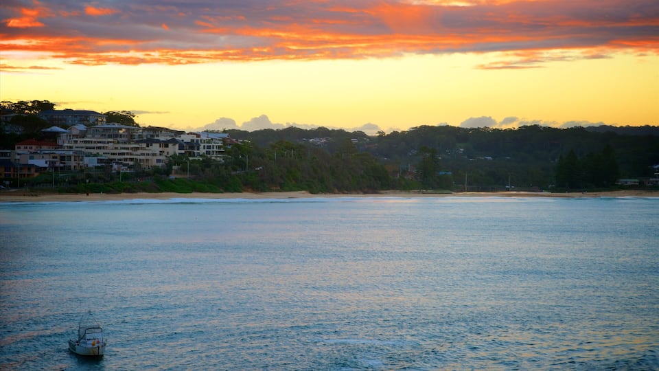 A coastal scene with a boat on calm waters, a beach, and a row of buildings in the background.