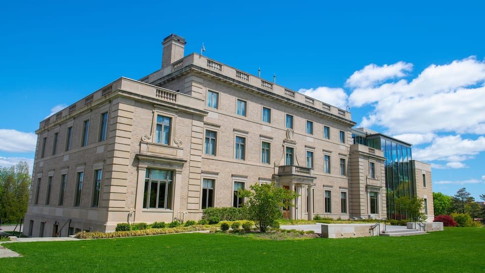 A large, historic building with a modern glass extension, surrounded by a well-maintained lawn and mature trees.