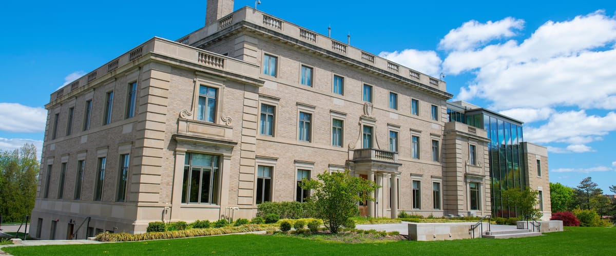 A large, historic building with a modern glass extension, surrounded by a well-maintained lawn and mature trees.