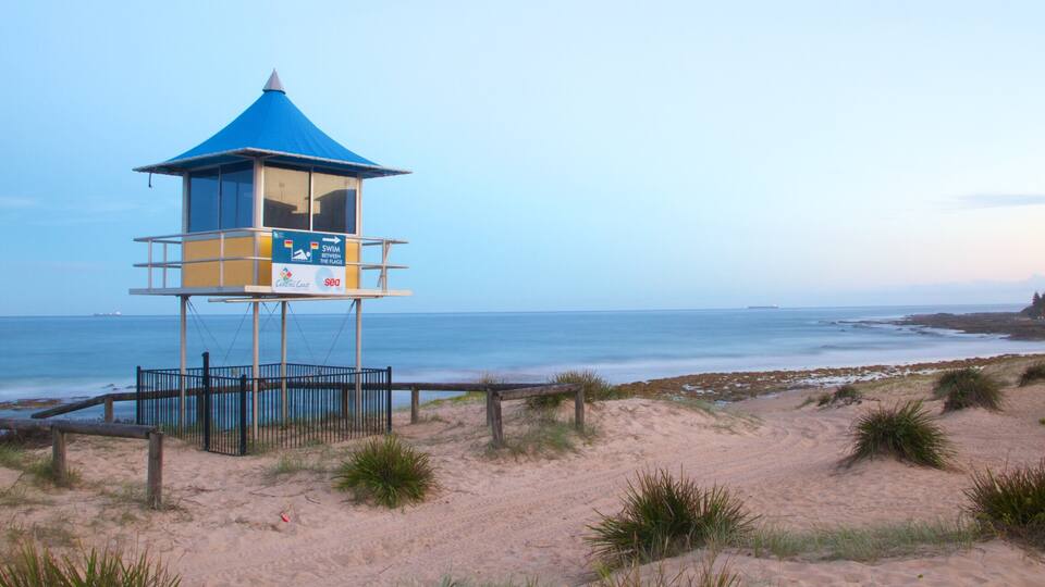 A lifeguard tower with a blue roof and a sign indicating a swimming area between flags.