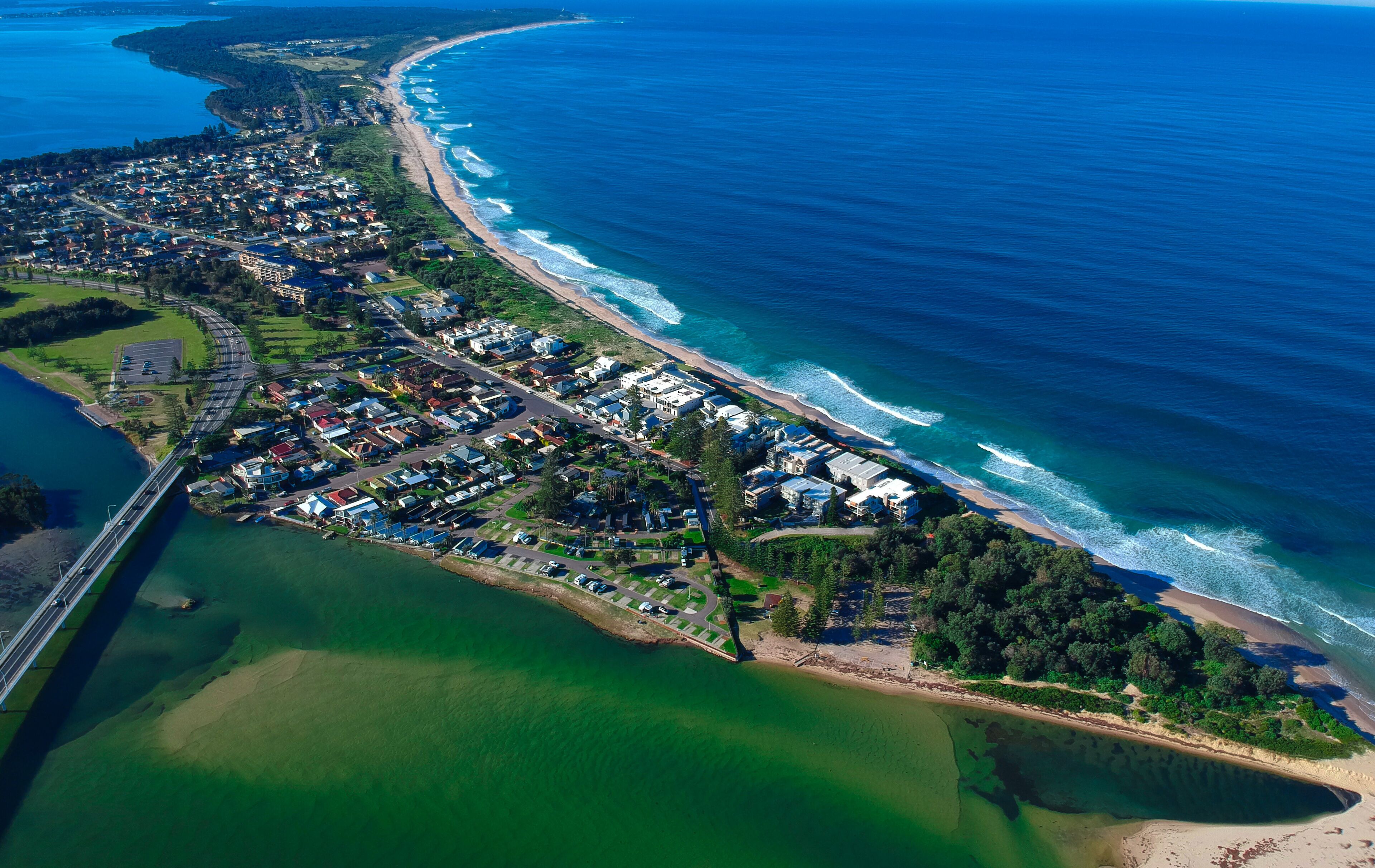 An aerial view of a coastal residential area with a beach, a bridge, and a marina.