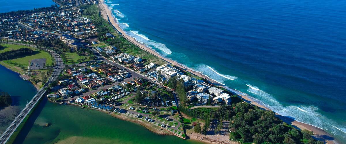 Vista aérea de una zona residencial costera con una playa, un puente y un puerto deportivo.