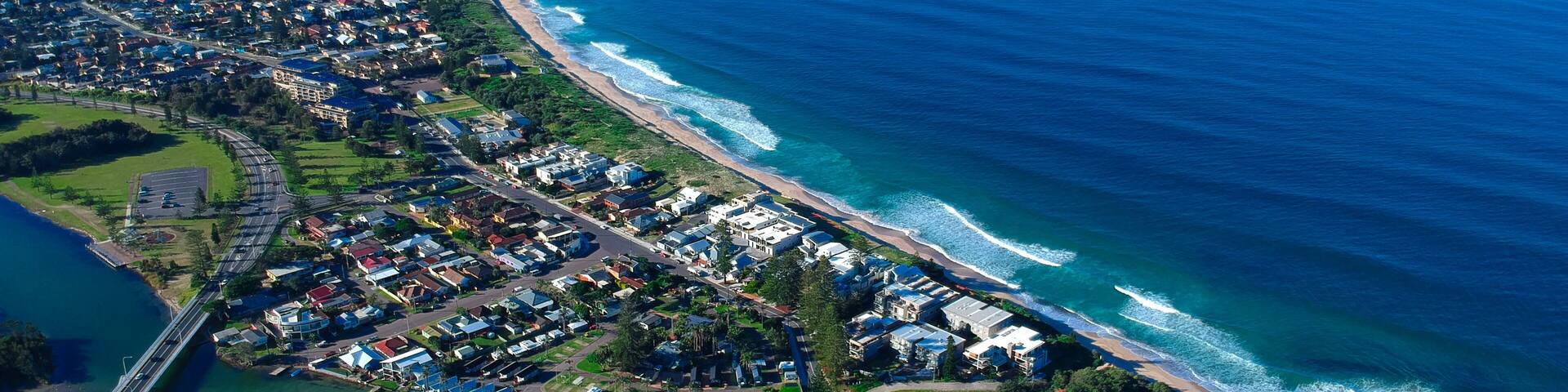 An aerial view of a coastal residential area with a beach, a bridge, and a marina.