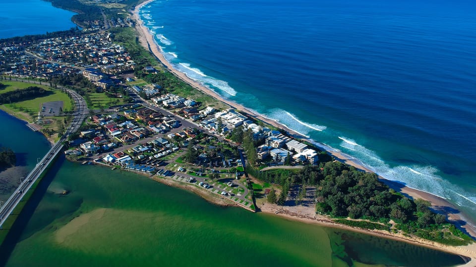 An aerial view of a coastal residential area with a beach, a bridge, and a marina.