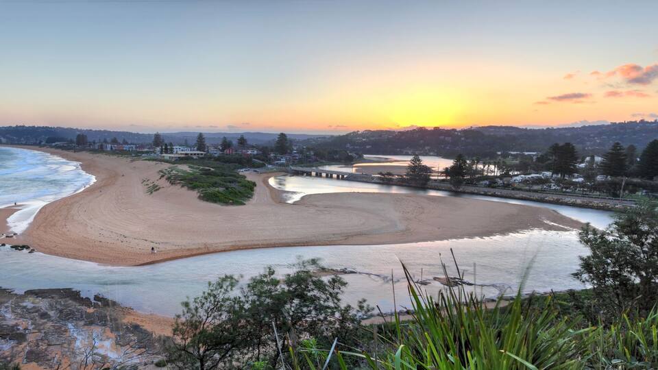 A beach with a curved shoreline, a river, and a sunset.