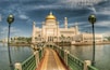 A large white building with a golden dome, surrounded by water and palm trees.
