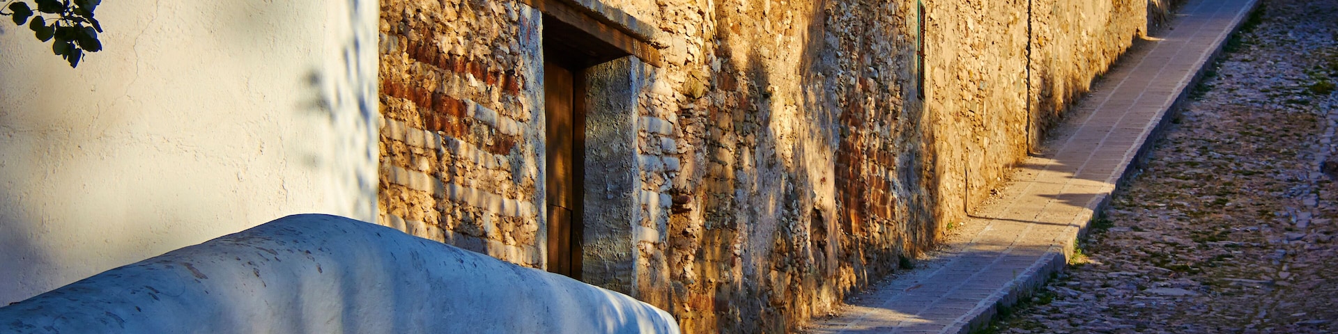Una calle empedrada con un muro blanco y un muro de piedra con un vano.