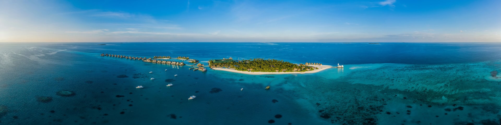 Panoramic aerial view of a luxury resort with boats anchored along the coast on Raa Atoll in the Laccadive Sea, Maldives archipelagos.